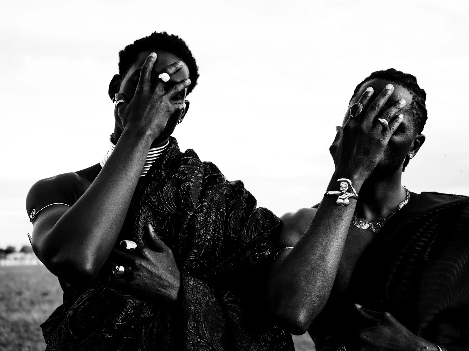 Two men in dark robes cover their faces with ringed hands.