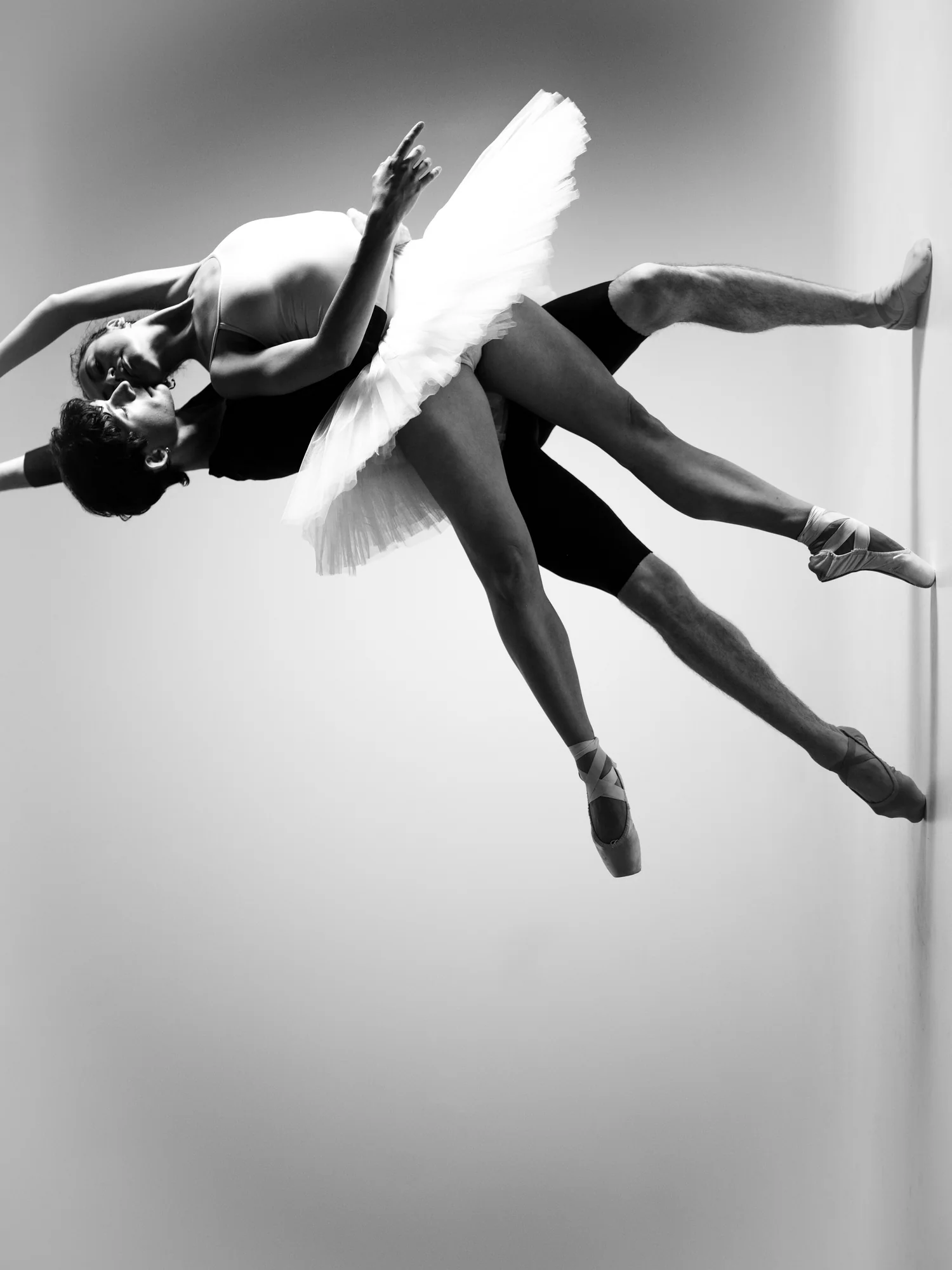 Two dancers float sideways across the frame, a ballerina in a tutu carried against her partner.