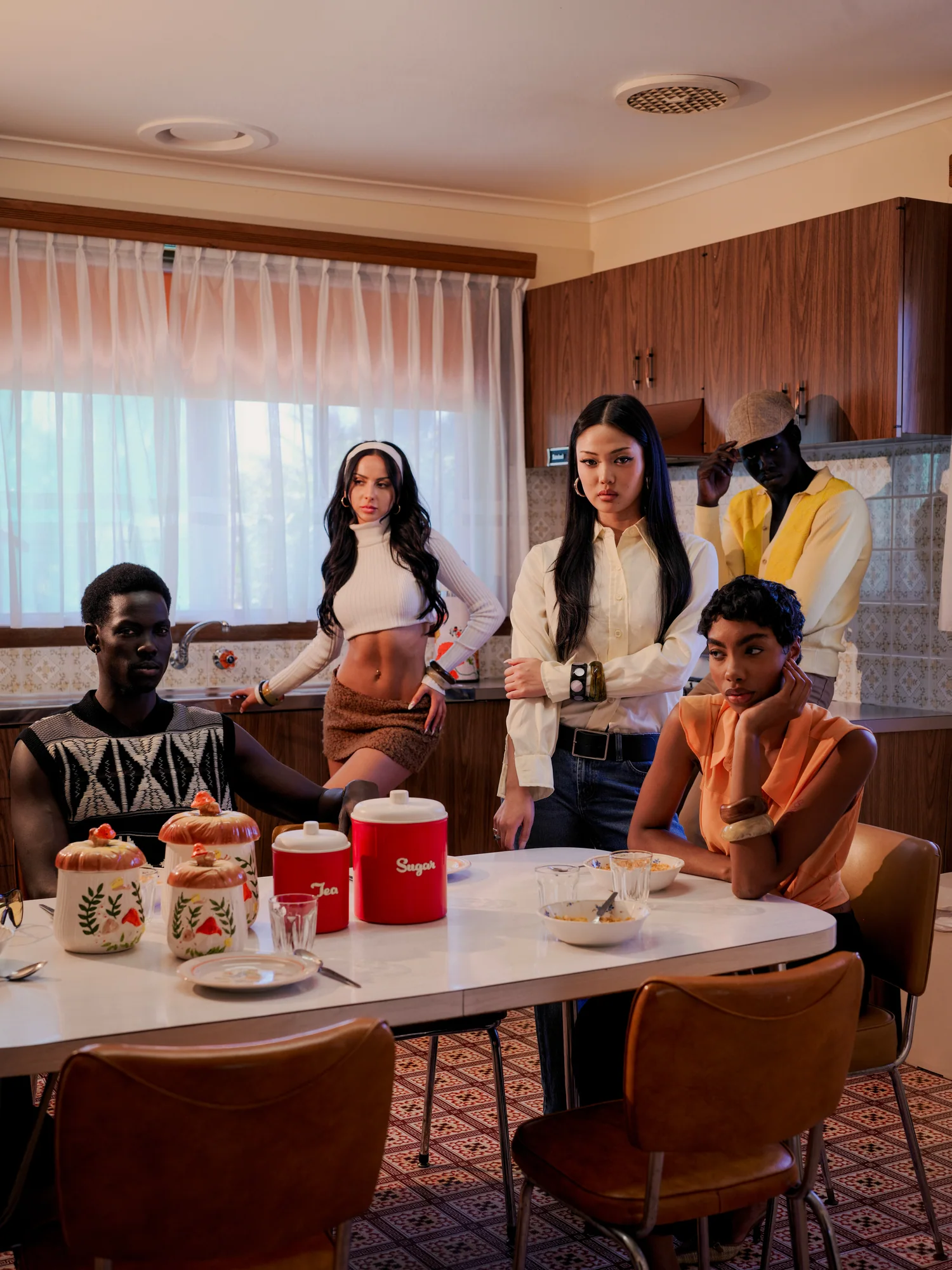 Five people in seventies dress gather around a kitchen table set with vintage canisters.