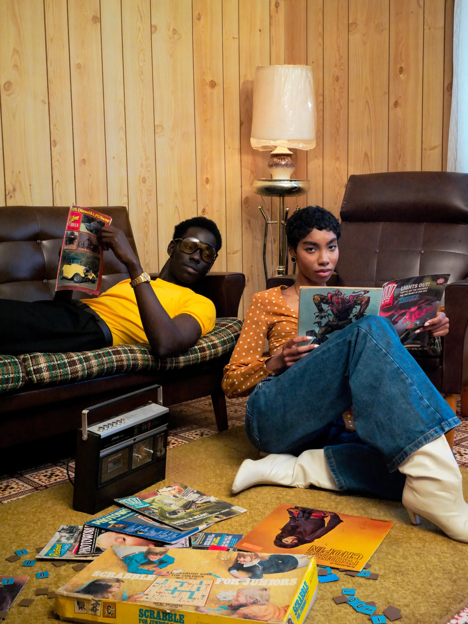 A man on a leather sofa and a woman on the floor read magazines in a wood-panelled lounge.