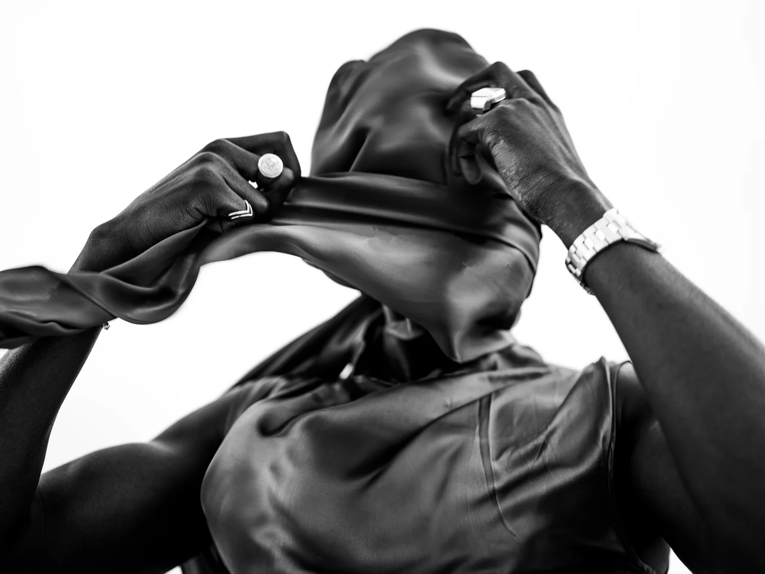 A figure seen from behind draws satin fabric over their head.