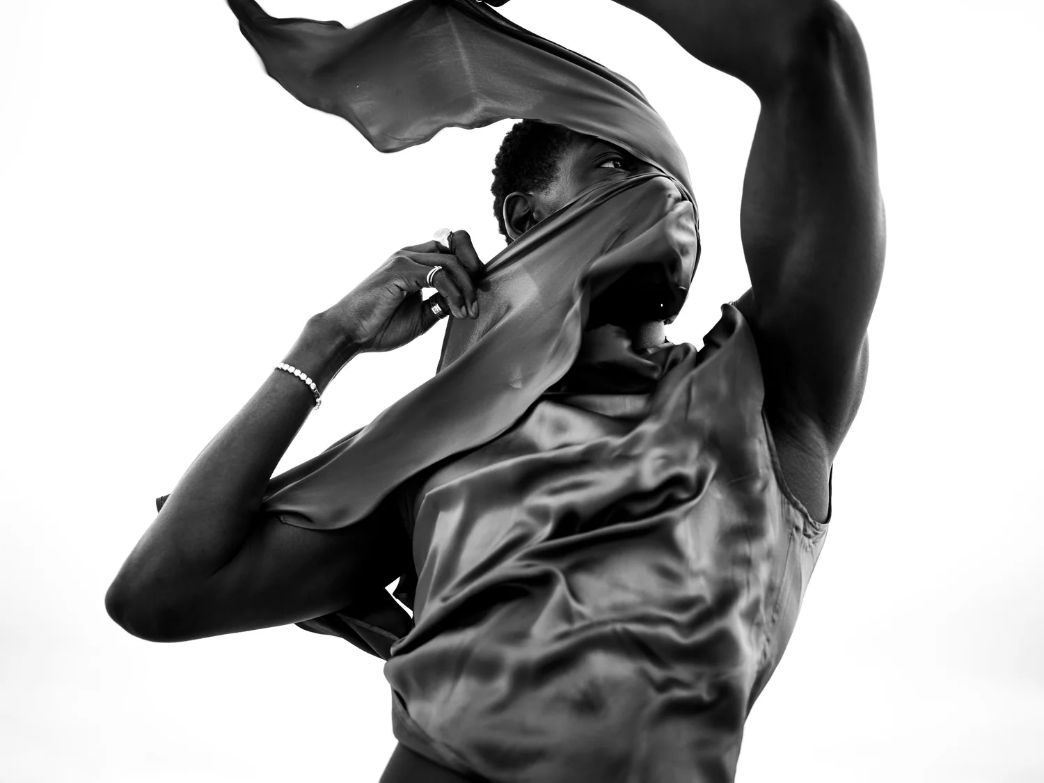 A man pulls his satin collar over his face as fabric whips above him.