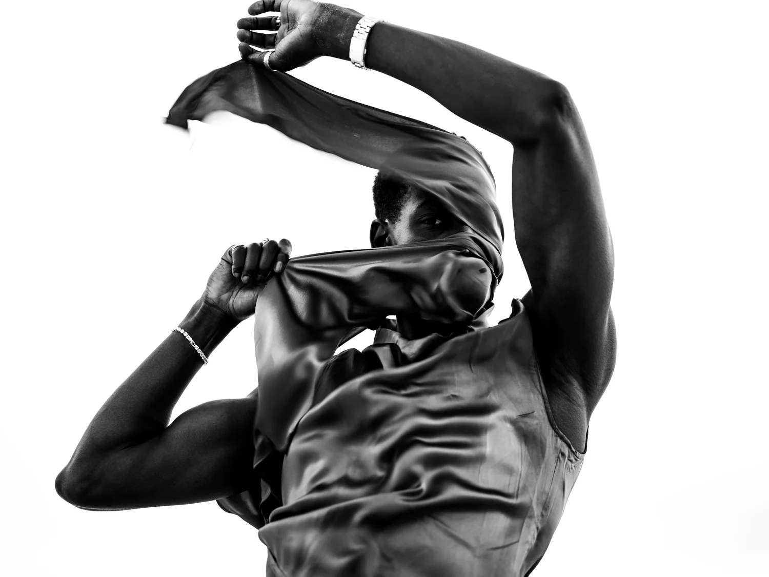 A man arches one arm overhead, drawing satin across his face.